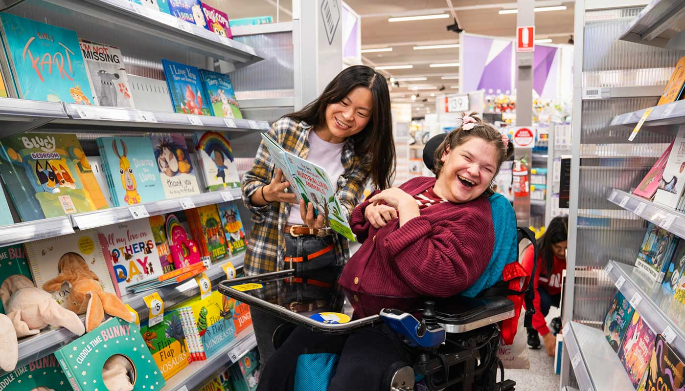 Person with disability in wheelchair laughing with carer in book shop