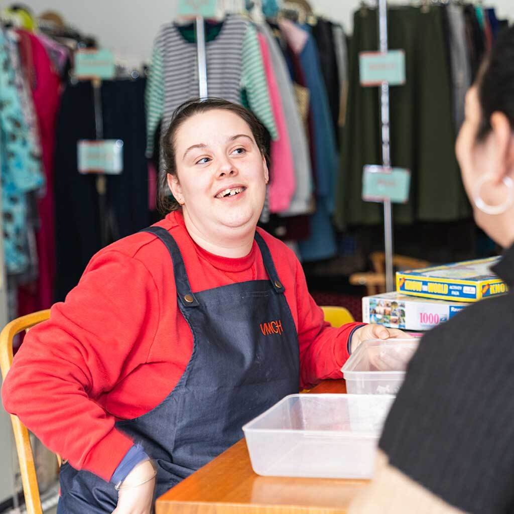 a woman sits inside an op shop and smiles