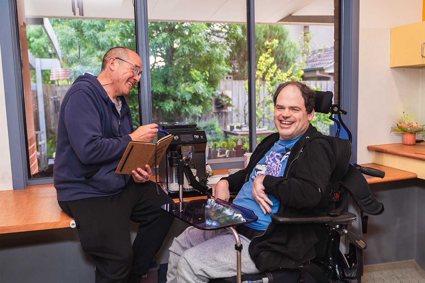 A person using a wheelchair smiles while talking with a support worker during a one-to-one support session.
