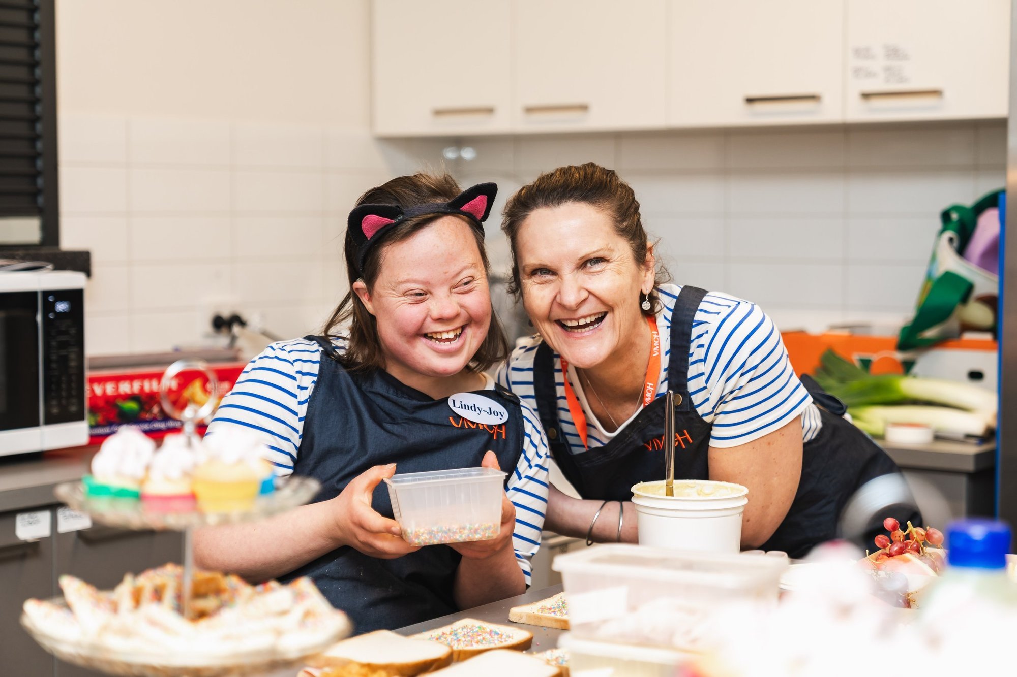 Two women making fairy bread in a kitchen.