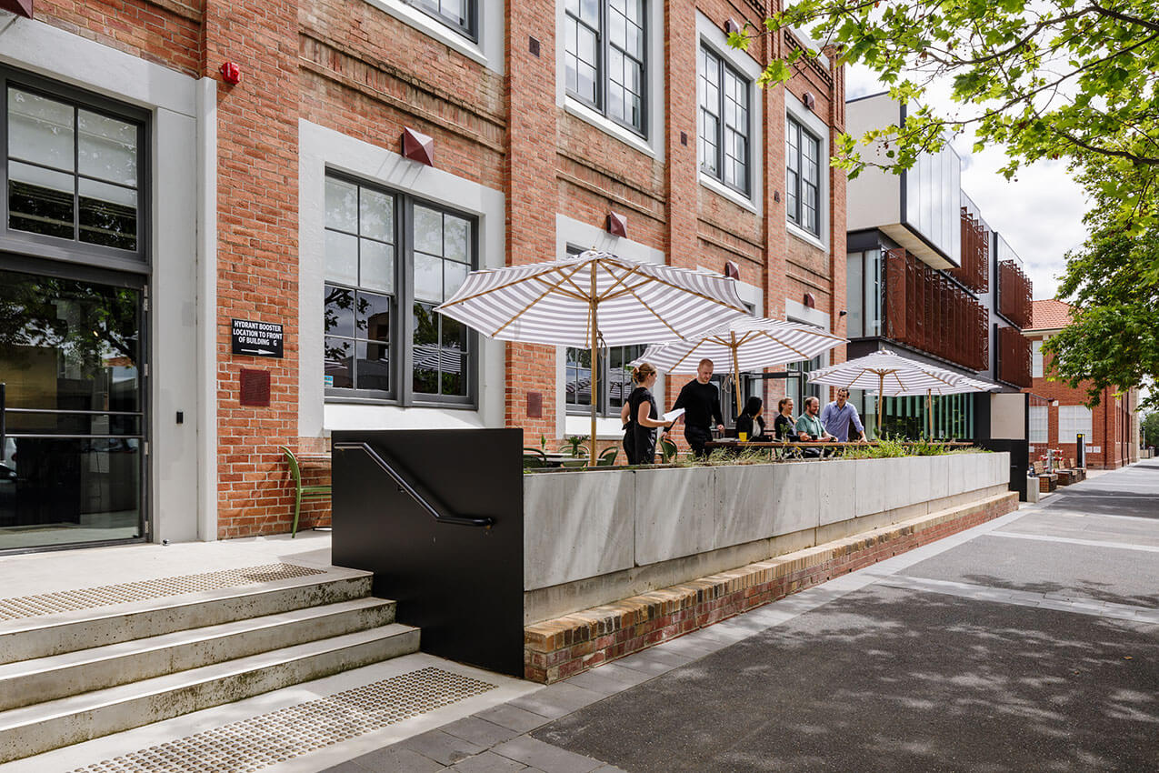 Brick building with large windows and four market umbrellas out the front