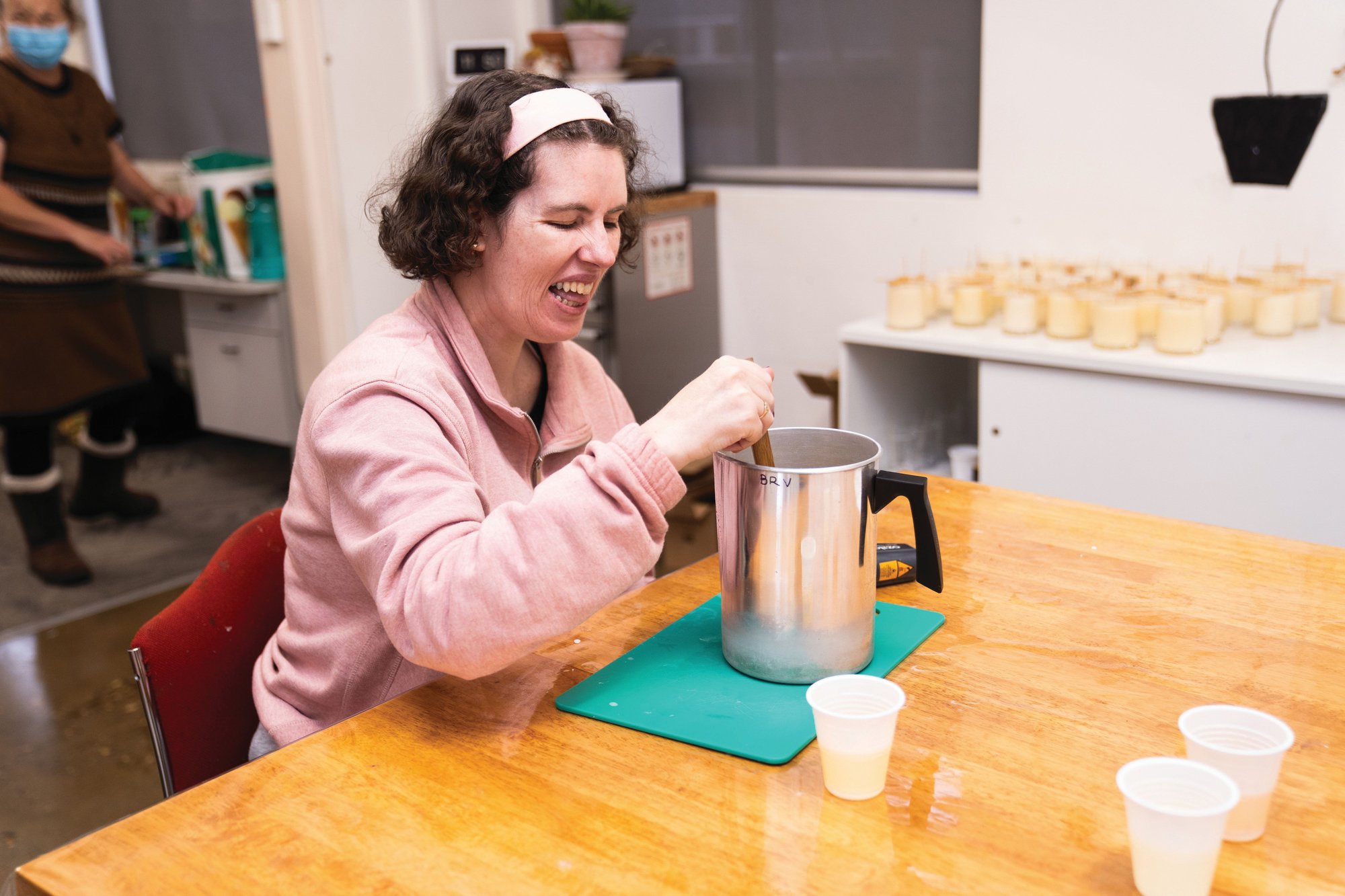 Woman wearing pink jumper and headband stirring liquid in silver jar