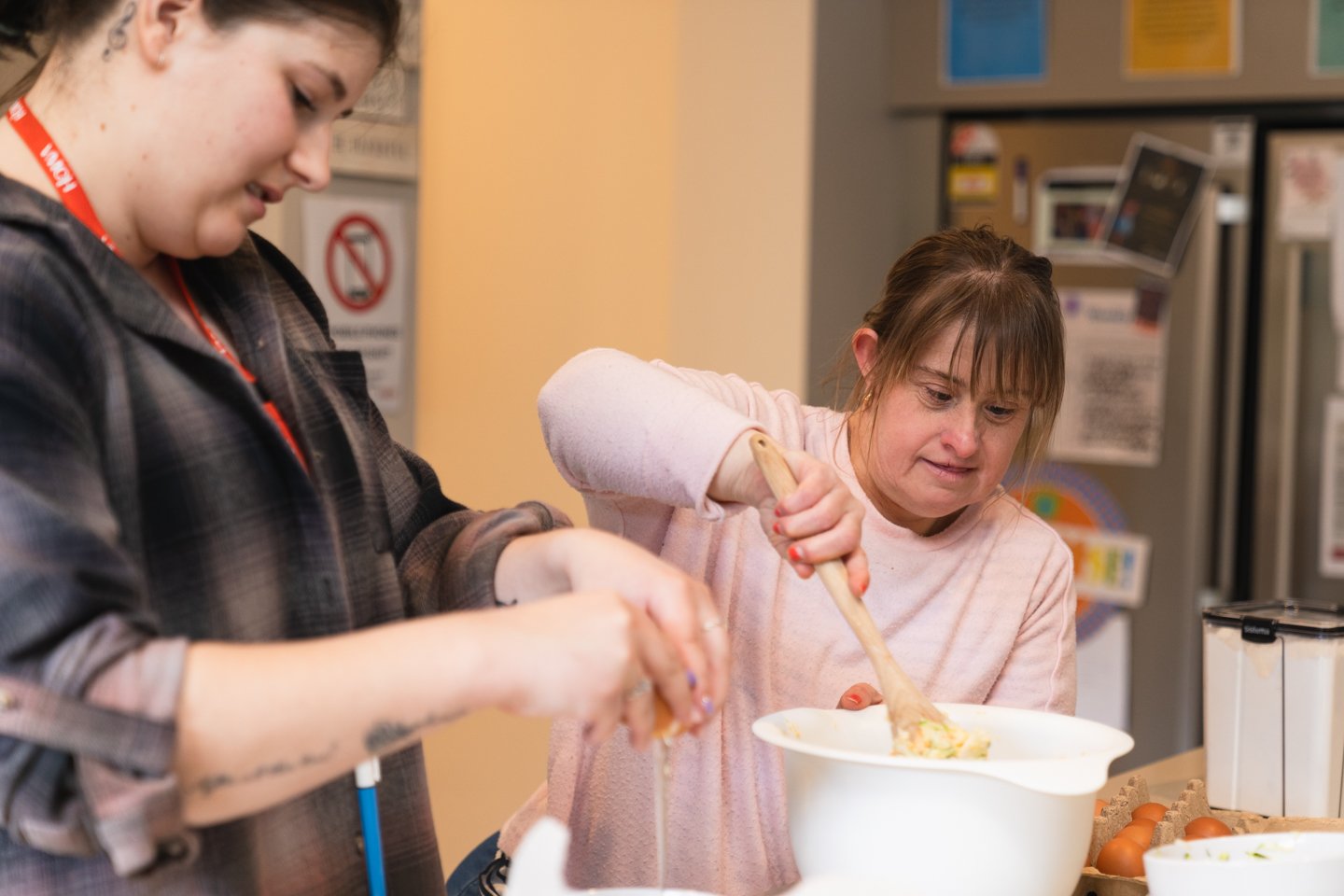 A support worker assisting a person with a disability to prepare a meal in the kitchen.