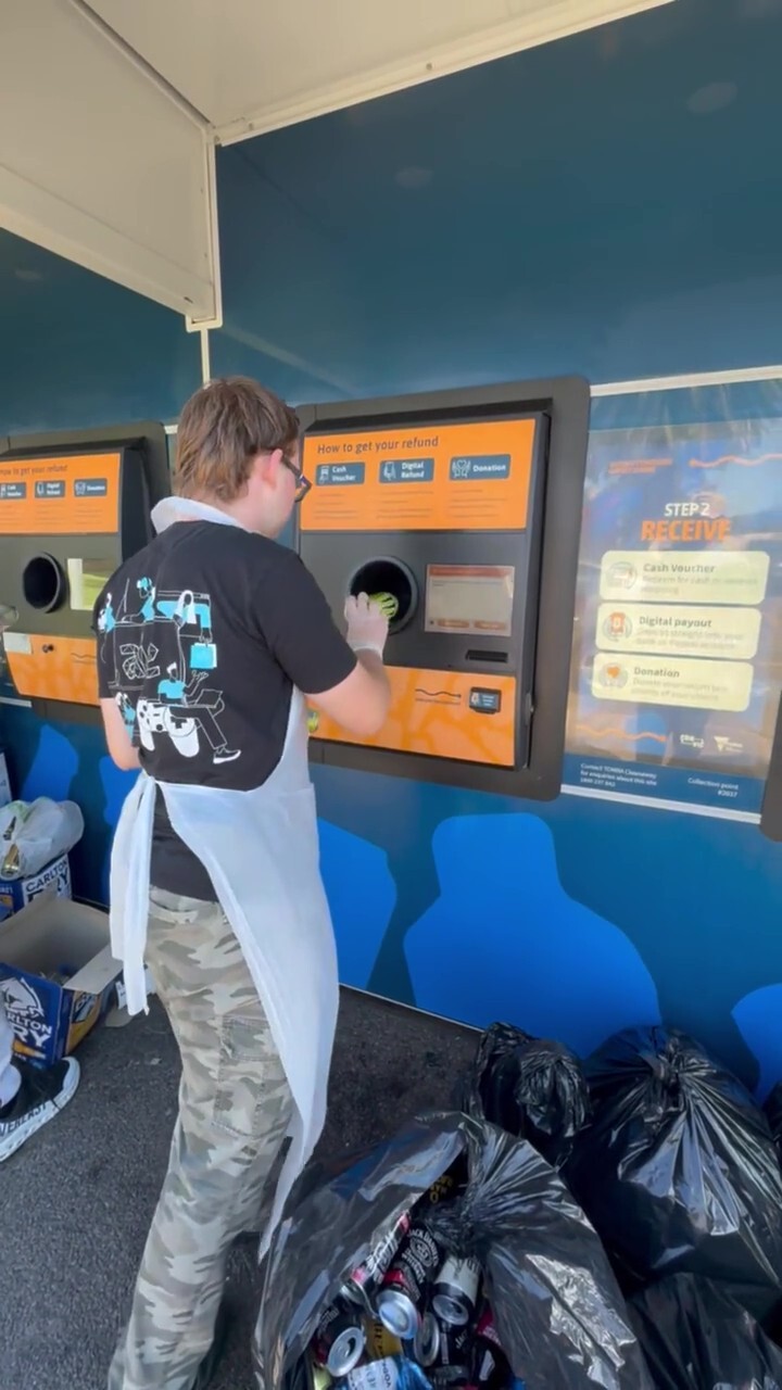 A male wearing a white apron feeding cans into a machine
