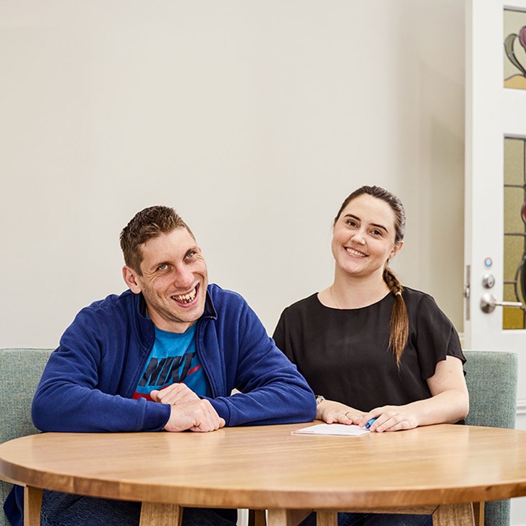 A man and a woman sit behind a table and smile at the camera