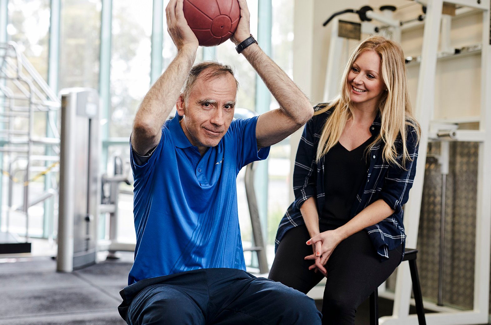 A person participates in a guided exercise activity with support from a worker, receiving assistance during a health or wellbeing appointment.