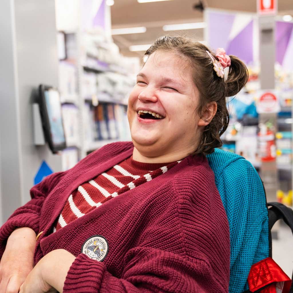 A woman in a wheel chair laughing in a shop aisle.