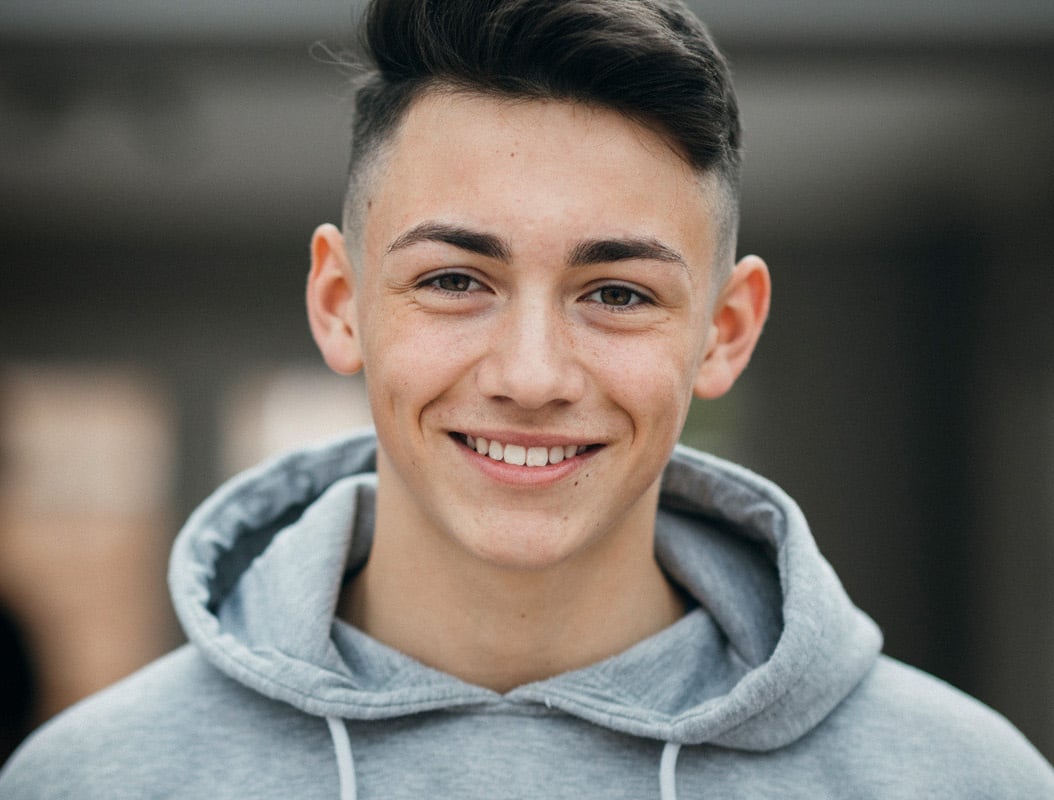 A teenage boy wearing a hoodie smiling.