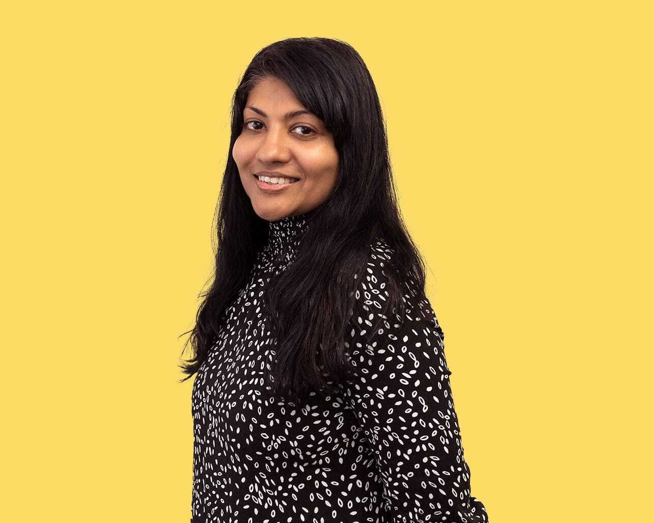 A woman in front of a yellow background smiles at the camera