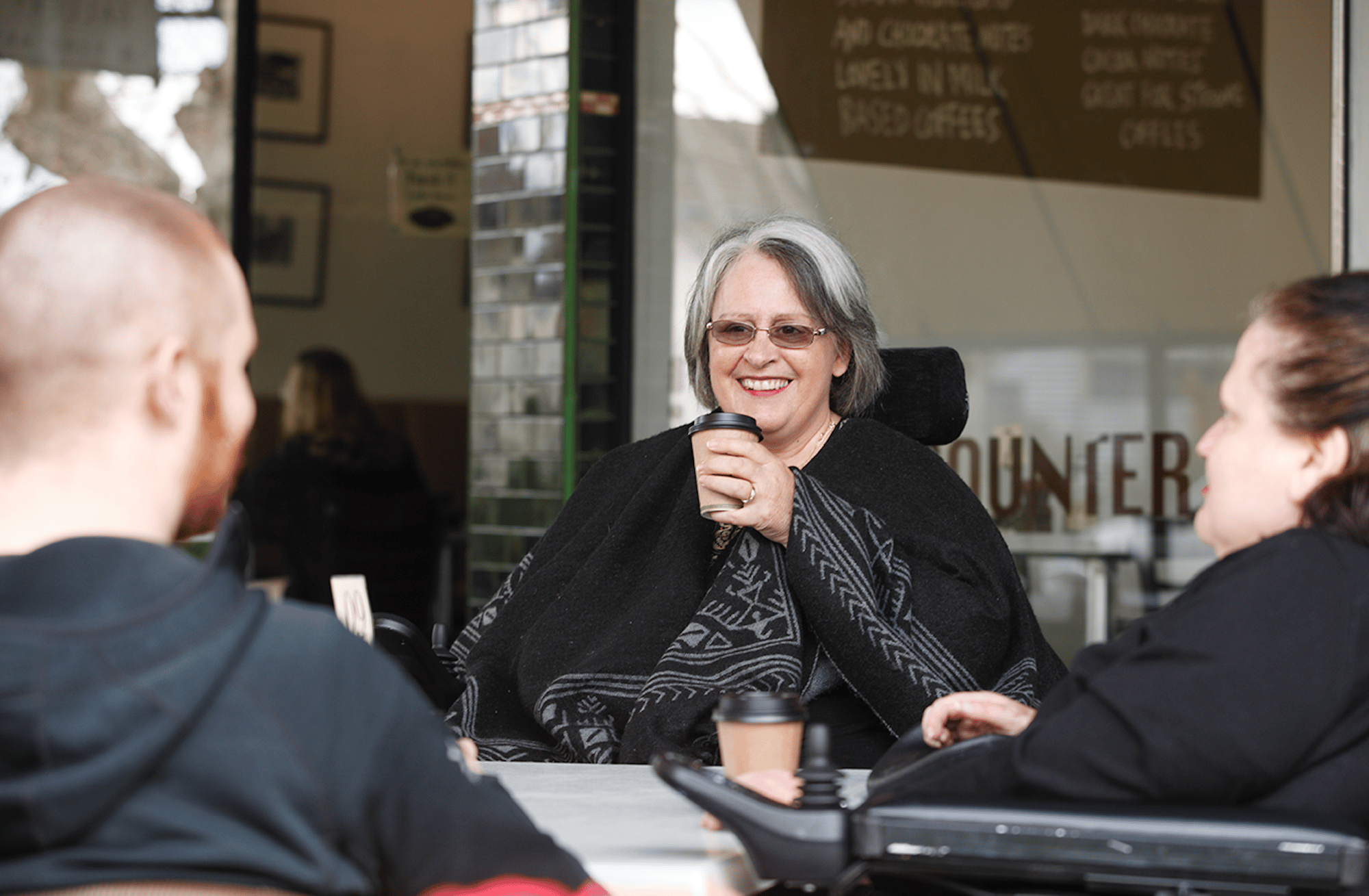 A person using a wheelchair enjoying a coffee at an outdoor café with others.
