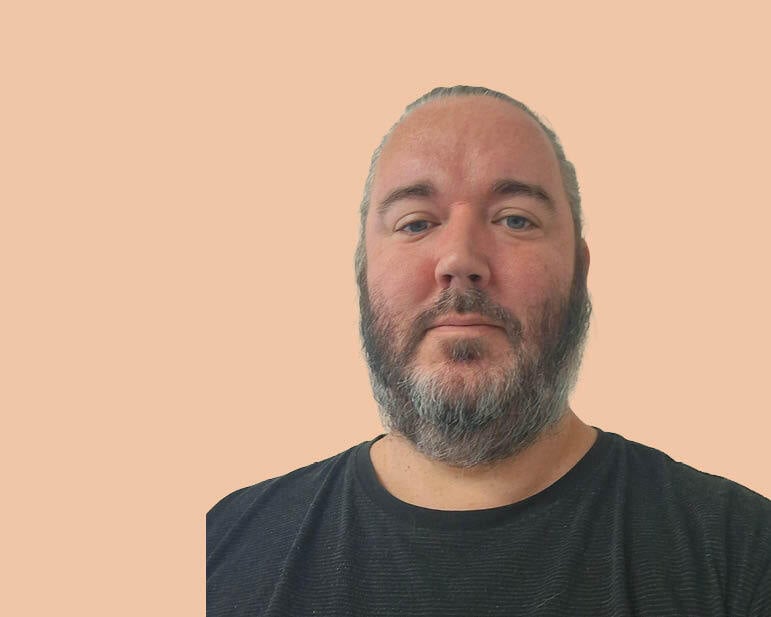 A man with a beard looks at the camera
