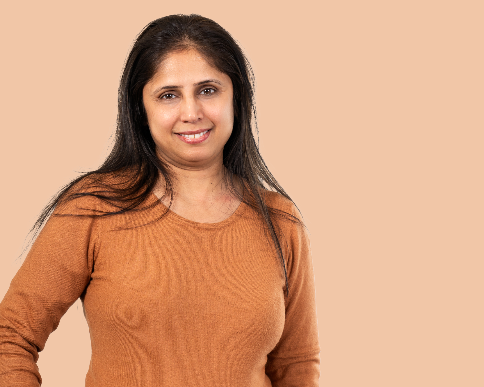 A woman wearing a tan coloured top smiles at camera